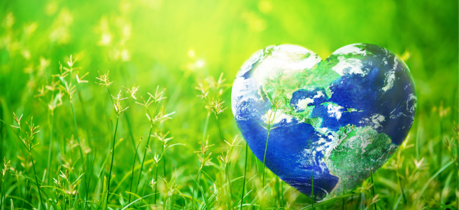 A small heart-shaped planet earth, sitting on sunlit grass.