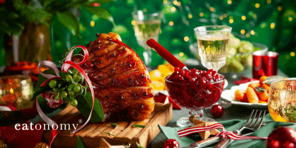 A Christmas table with ham, berries, wine, cutlery and candles, with the words "Season's Eatings".