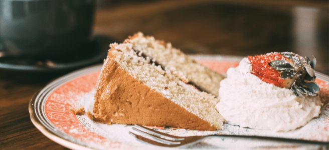 A piece of vanilla sponge came on a plate with a dollop of cream, a strawberry and a small fork.